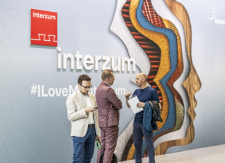 interzum 2025 | Η Καινοτομία και η Βιωσιμότητα στο Επίκεντρο Άνδρας περπατά μπροστά από έναν μεγάλο τοίχο με το λογότυπο της έκθεσης Interzum 2025 και το hashtag #ILoveMyInterzum, σε έναν φωτεινό και σύγχρονο εκθεσιακό χώρο.