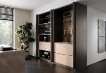 Σύστημα POCKET DOOR PB15 της Cinetto σε λειτουργία, με ξύλινες πόρτες που αποκαλύπτουν σύγχρονο χώρο κουζίνας με ηλεκτρικές συσκευές και πάγκο εργασίας.